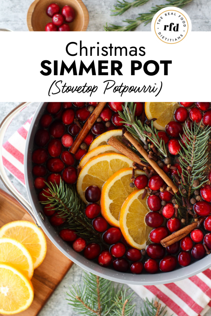 Overhead view pot filled with cranberries, orange slices, pine sprigs, cinnamon sticks and water for a stovetop potpourri.