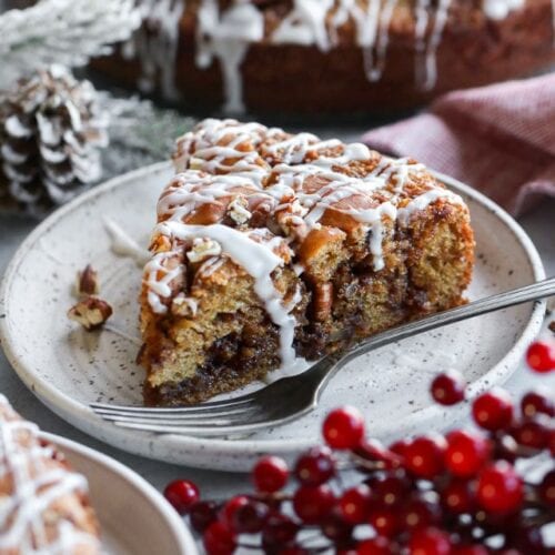 Slice of cinnamon roll coffee cake with white icing drizzled on top plated with fork.