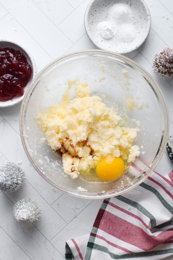 Sugar and butter creamed together in clear glass mixing bowl with egg added in