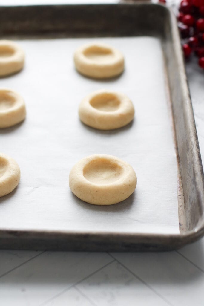 Thumbprint cookie dough with indent in middle lined up on parchment-covered baking sheet.