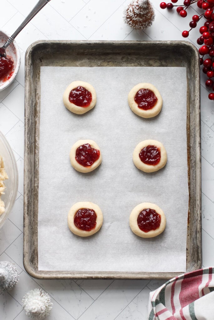 Overhead view raspberry thumbprint cookies on parchment-covered baking sheet.