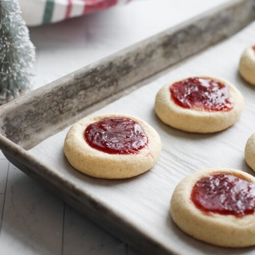 Raspberry Thumbprint cookies lined up on parchment-covered baking sheet.