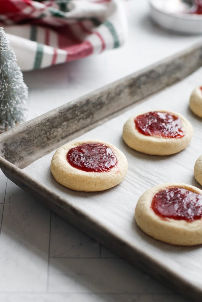 Thumbprint cookies filled with raspberry jam freshly baked on a baking sheet.