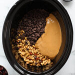 Overhead view black crockpot filled with ingredients for peanut clusters with chocolate.