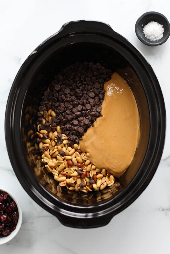 Overhead view black crockpot filled with all ingredients for peanut butter chocolate clusters.
