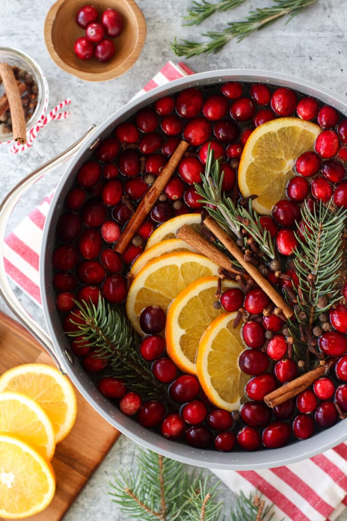 Overhead view pot filled with all ingredients for Christmas Simmer Pot, fresh cranberries, orange slices, pine sprigs, and cinnamon sticks. 