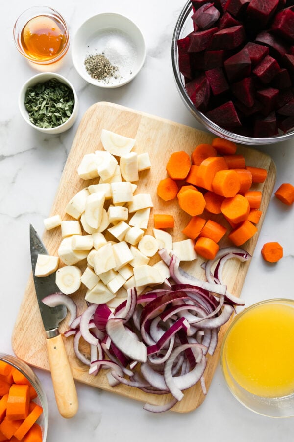 All ingredients for roasted root vegetables arranged together in small bowls and on a cutting board.