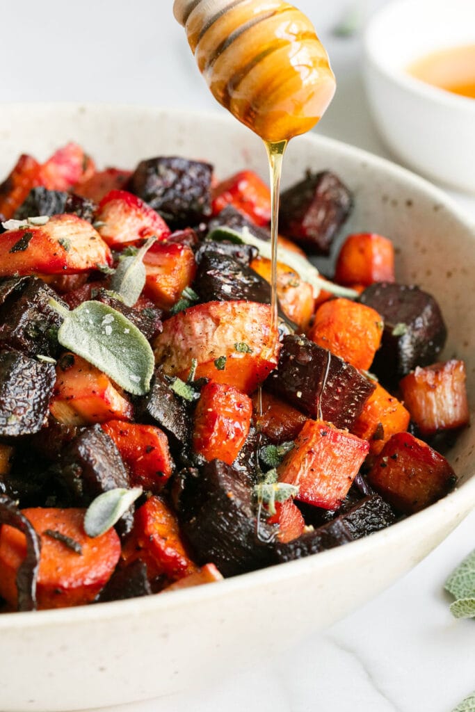 Honey being drizzled over roasted root vegetables in a serving bowl