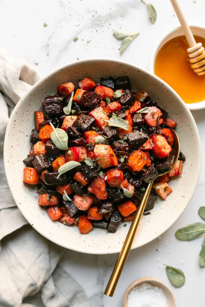 Roasted root vegetables in a shallow bowl topped with honey and small sage leaves. 