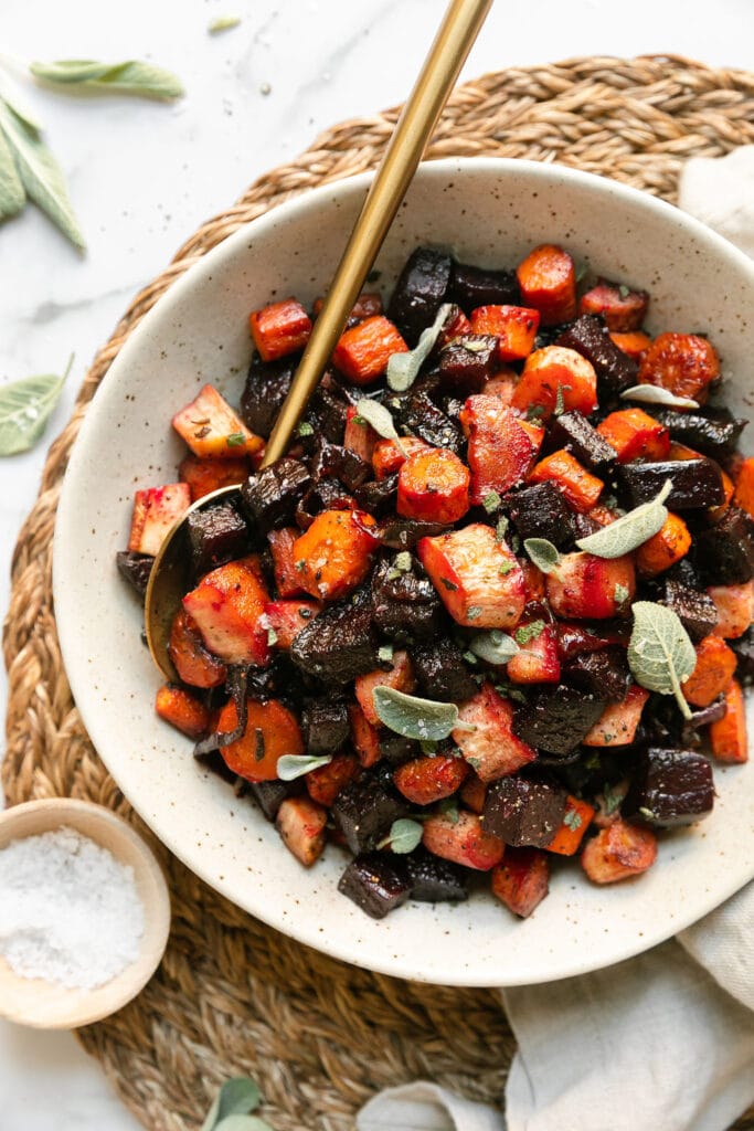 Honey sage roasted root vegetables in a shallow white serving bowl with a gold spoon.