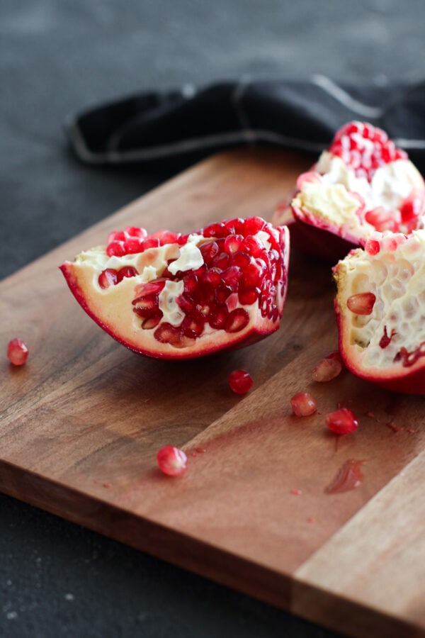 A fresh pomegranate cut into sections laying on skin-side down on a wooden cutting board.
