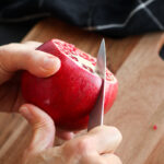A fresh pomegranate being sliced down the sides to remove sections 