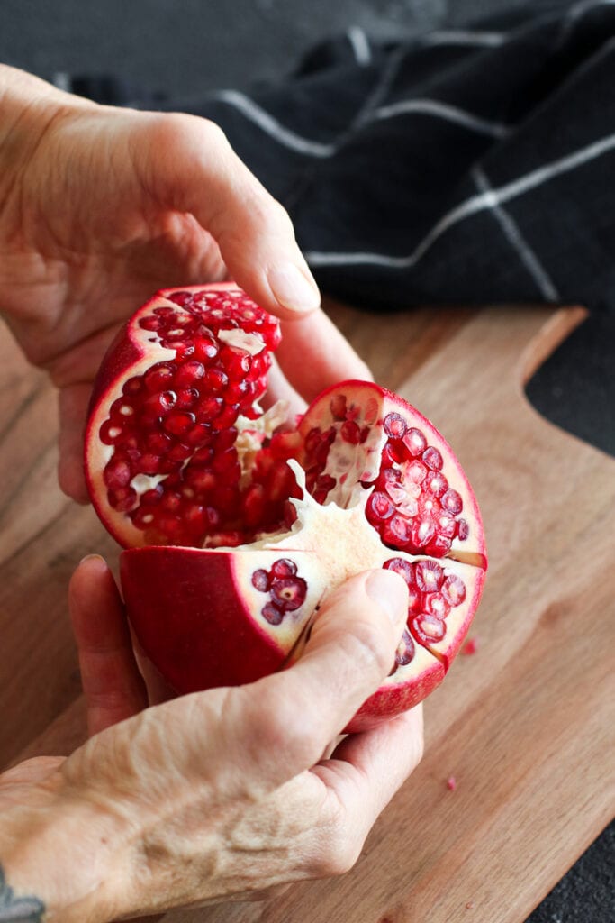 A fresh pomegranate cut into sections being broken apart over a wooden cutting board.