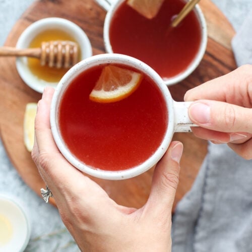 Two hands holding mug filled with peach tea, lemon slice floating in tea.