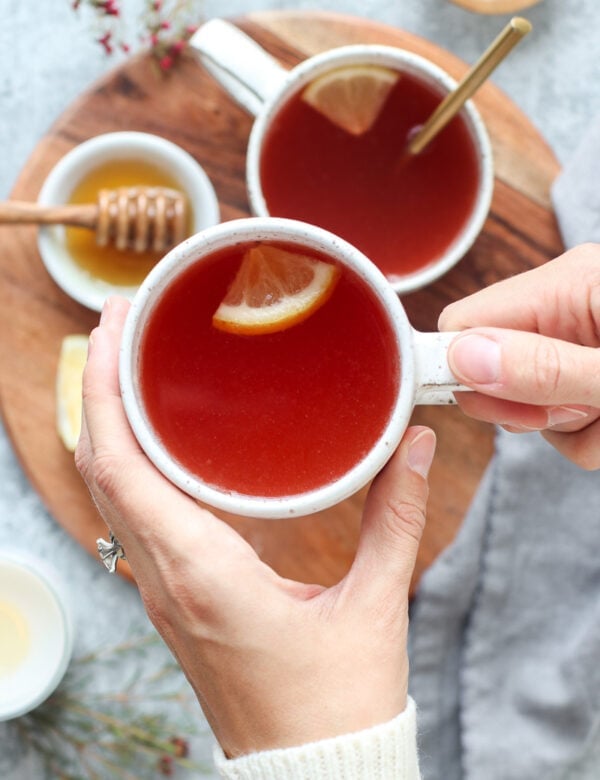 Two hands holding mug filled with peach tea, lemon slice floating in tea.