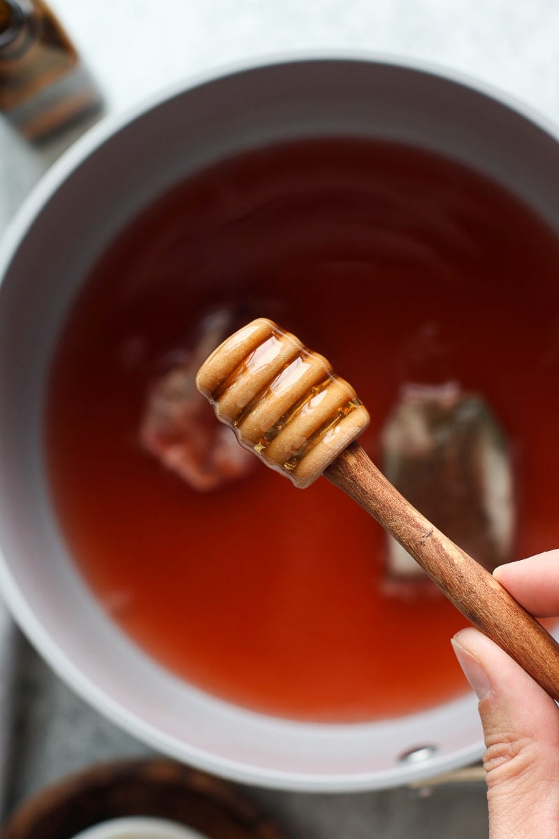 Close up view honey dipper coated in honey over a saucepan of steeping Medicine Ball Tea