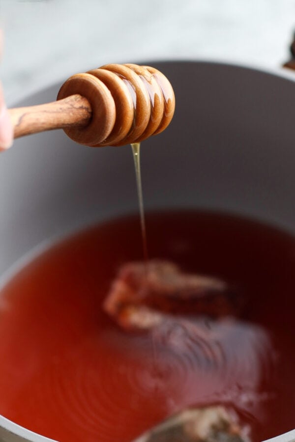 A honey dipper drizzling honey into a saucepan of Medicine Ball Tea steeping.