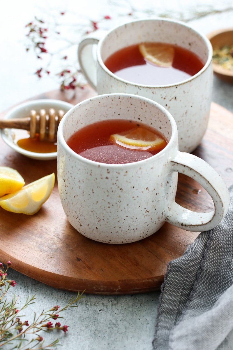 Two mugs filled with Starbucks Medicine Ball Tea on a round wooden tray, small bowl with honey and honey dipper on side.