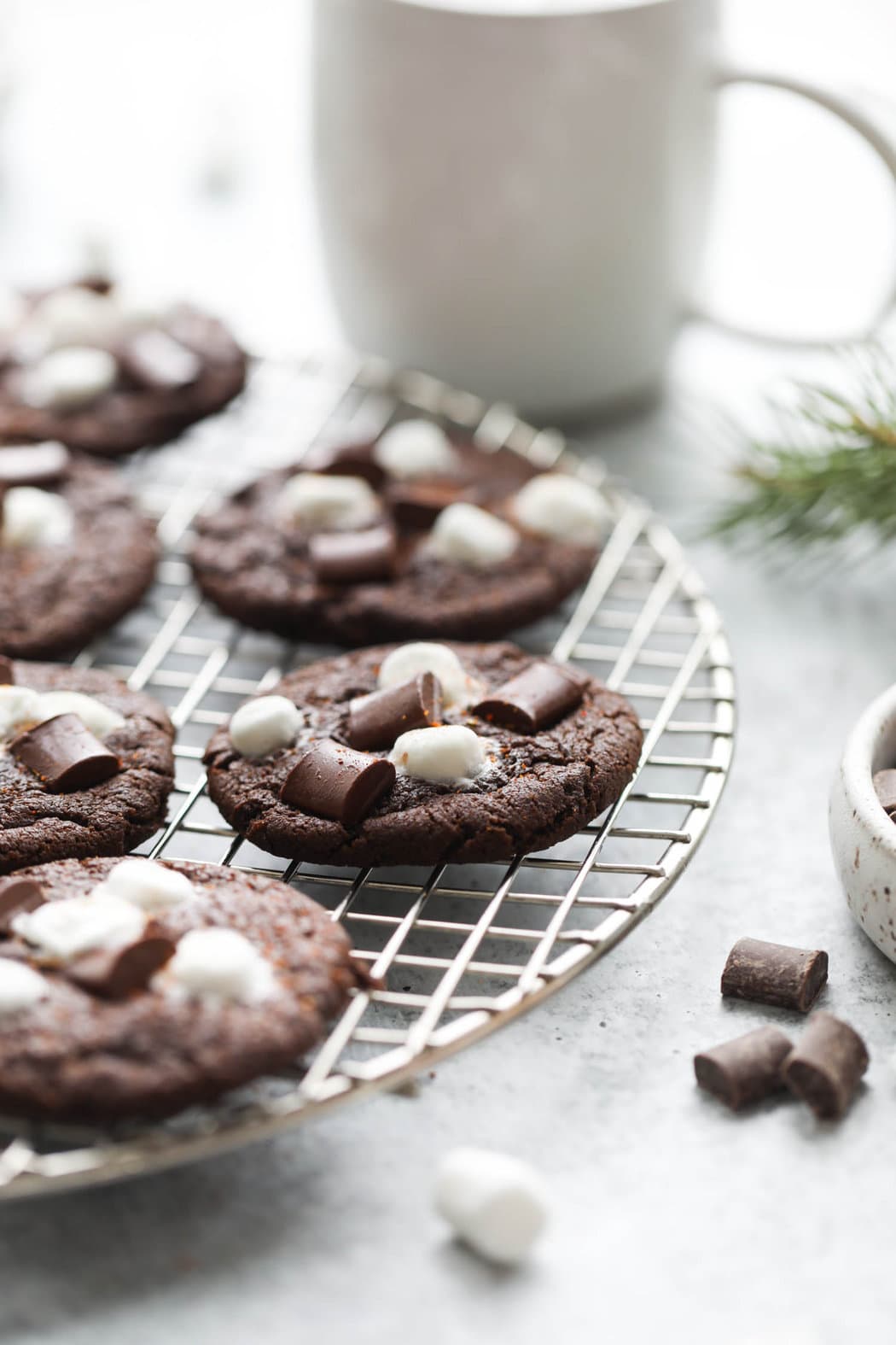 Close up side view Mexican hot chocolate cookie topped with melty mini marshmallows and chocolate chunks, sprinkled with cayenne pepper, on a cooling rack.