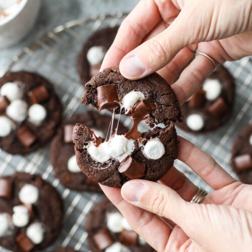 Two hands pulling apart a Mexican hot chocolate cookie with melty marshmallow stings between the halves.