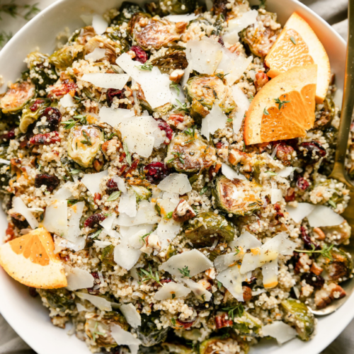Overhead view white serving bowl filled with Roasted Brussels Sprouts Quinoa Salad topped with shaved Parmesan cheese.
