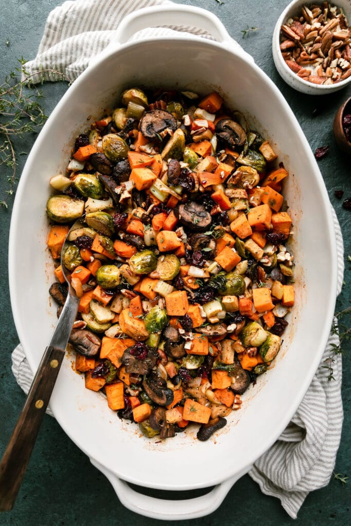 Overhead view white casserole dish filled with sweet potato unstuffing topped with pecans and cranberries, a silver serving spoon in stuffing.