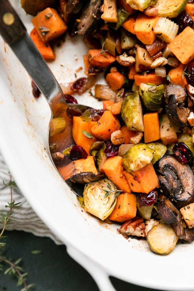 A silver serving spoon scooping up a serving of sweet potato unstuffing filled with dried cranberries, mushrooms, and Brussels sprouts. 