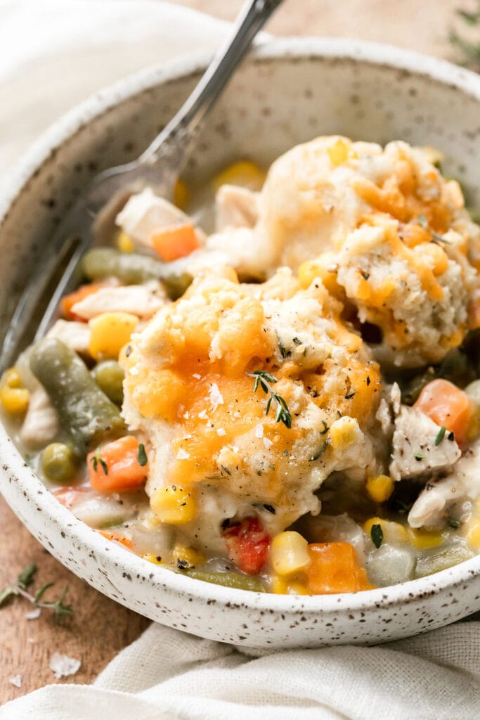 Close up view serving of chicken pot pie casserole in stone bowl topped with cheddar topped biscuit.