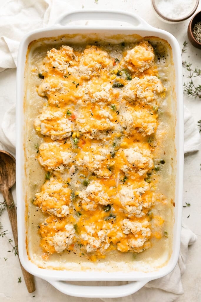 Baked chicken pot pie casserole in white baking dish topped with cheddar cheese topped drop biscuits.