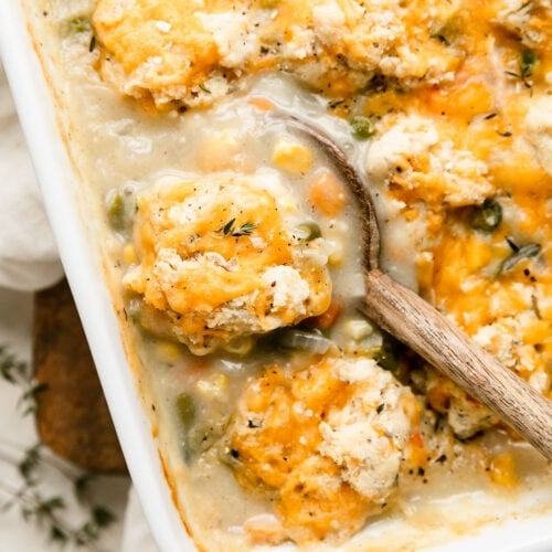 Wooden spoon scooping up serving of chicken pot pie casserole with drop biscuits on top.