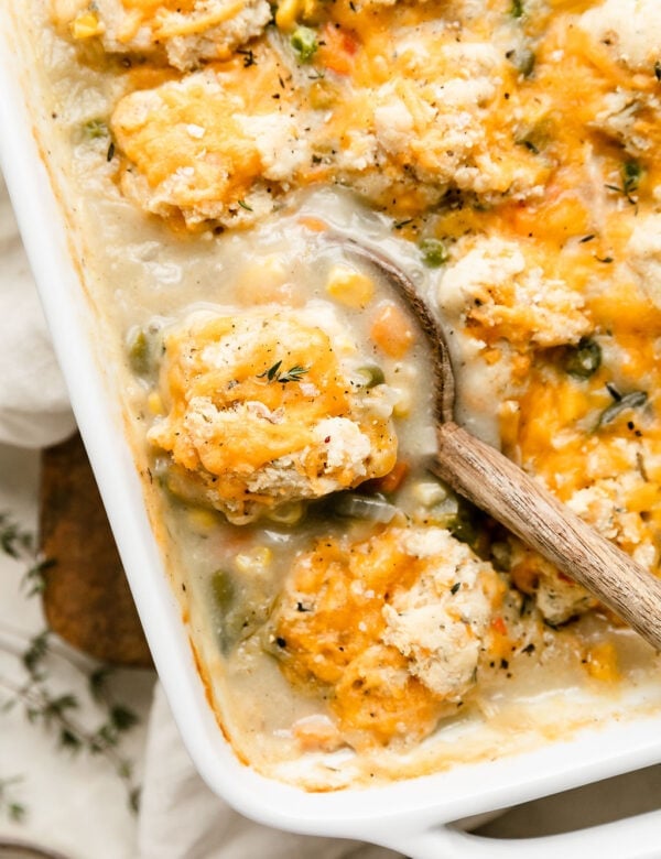 Wooden spoon scooping up serving of chicken pot pie casserole with drop biscuits on top.