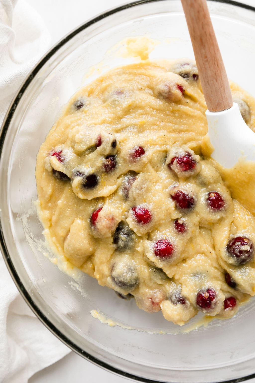 Cranberry orange olive oil cake batter in clear mixing bowl with spatula.