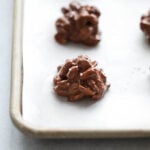 Side view crockpot chocolate peanut clusters lined up on baking sheet.