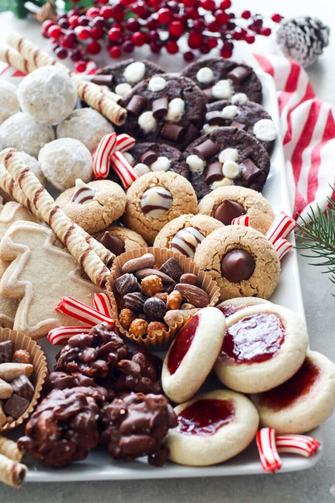 White tray filled with assortment of gluten free Christmas cookies and nuts and striped candy pieces.