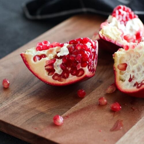 A pomegranate section filled with arils resting on a wooden cutting board.