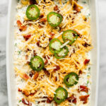 Overhead view white casserole dish filled with jalapeño popper dip, shredded cheese and jalapeño slices on top