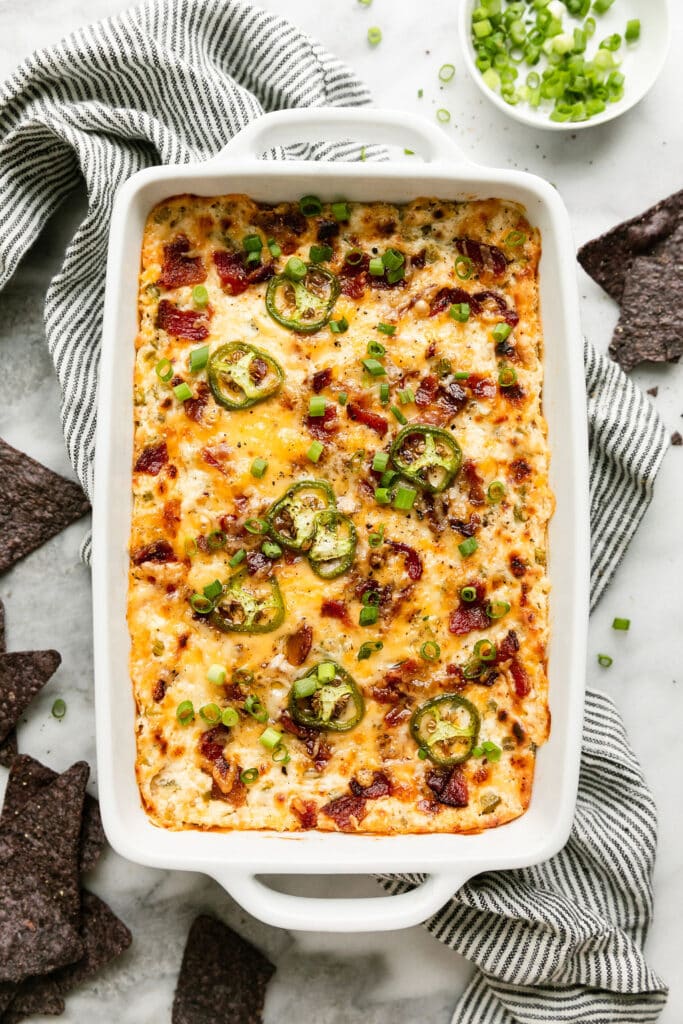 Overhead view long casserole dish filled with jalapeño popper dip topped with bacon, melted cheese, and jalapeño slices. 