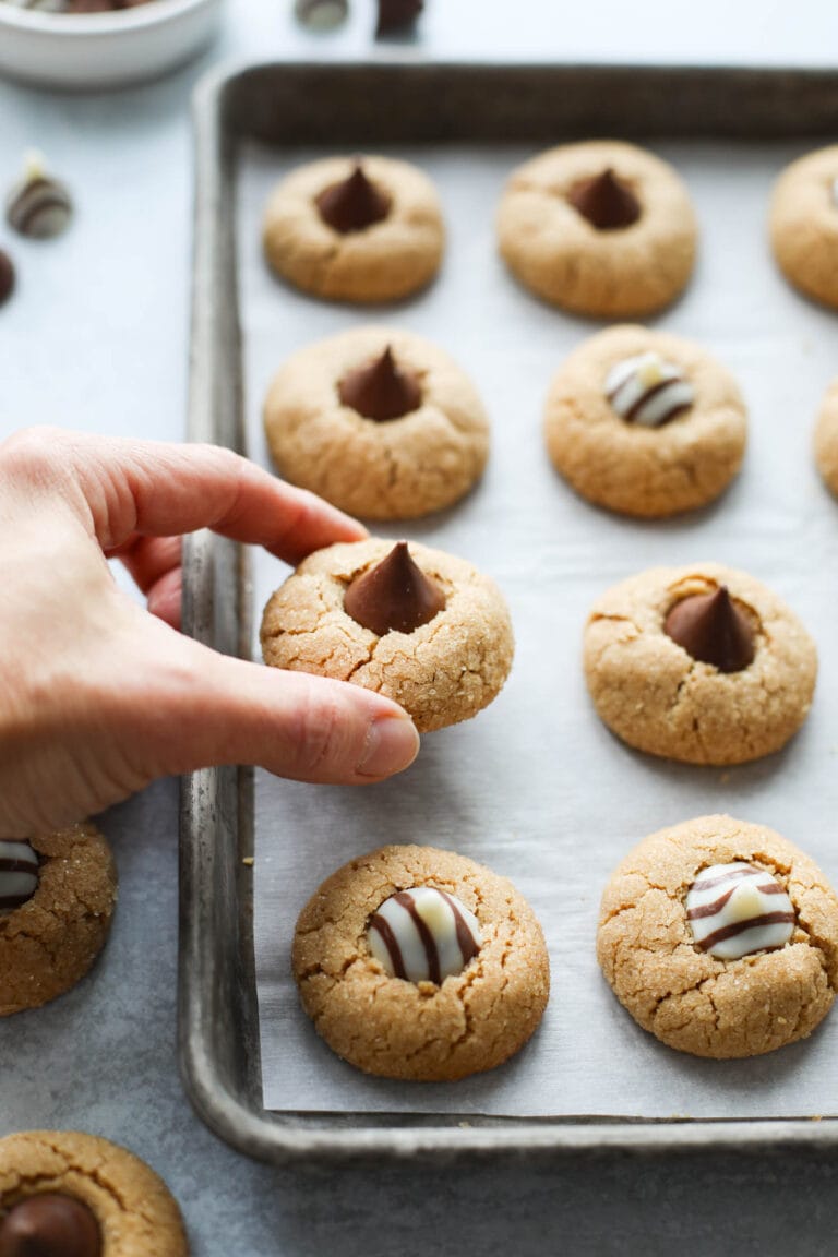 A hand lifting a peanut butter blossom from a baking sheet with lined up cookies. 
