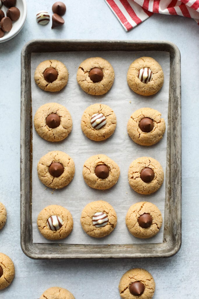 Overhead view baking sheet filled with lined up peanut butter blossoms with chocolate kisses and chocolate striped kisses in each cookie.