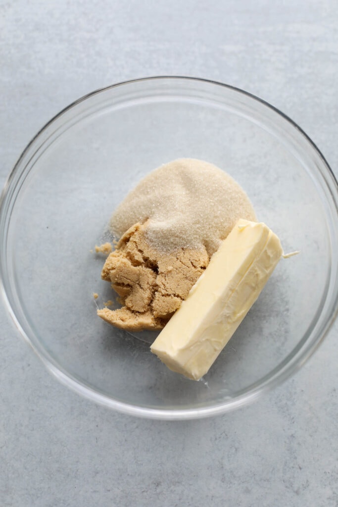Stick of butter, cane sugar, and brown sugar in a clear glass mixing bowl