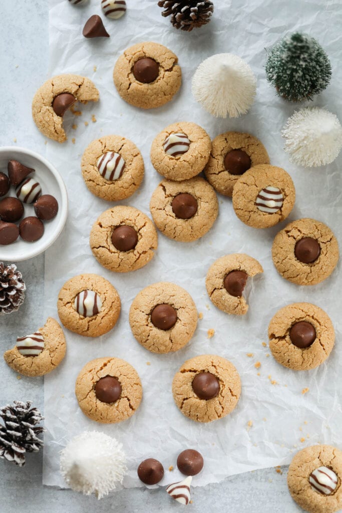 Peanut butter blossoms arranged together on parchment paper with Christmas decorations around.
