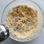 Cookie batter being mixed with hand mixer in clear glass bowl