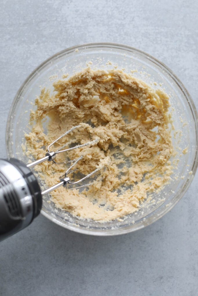 Butter and sugar creamed together for peanut butter blossoms in mixing bowl with hand mixer beaters in batter.