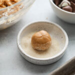 A ball of cookie dough in shallow bowl of cane sugar 