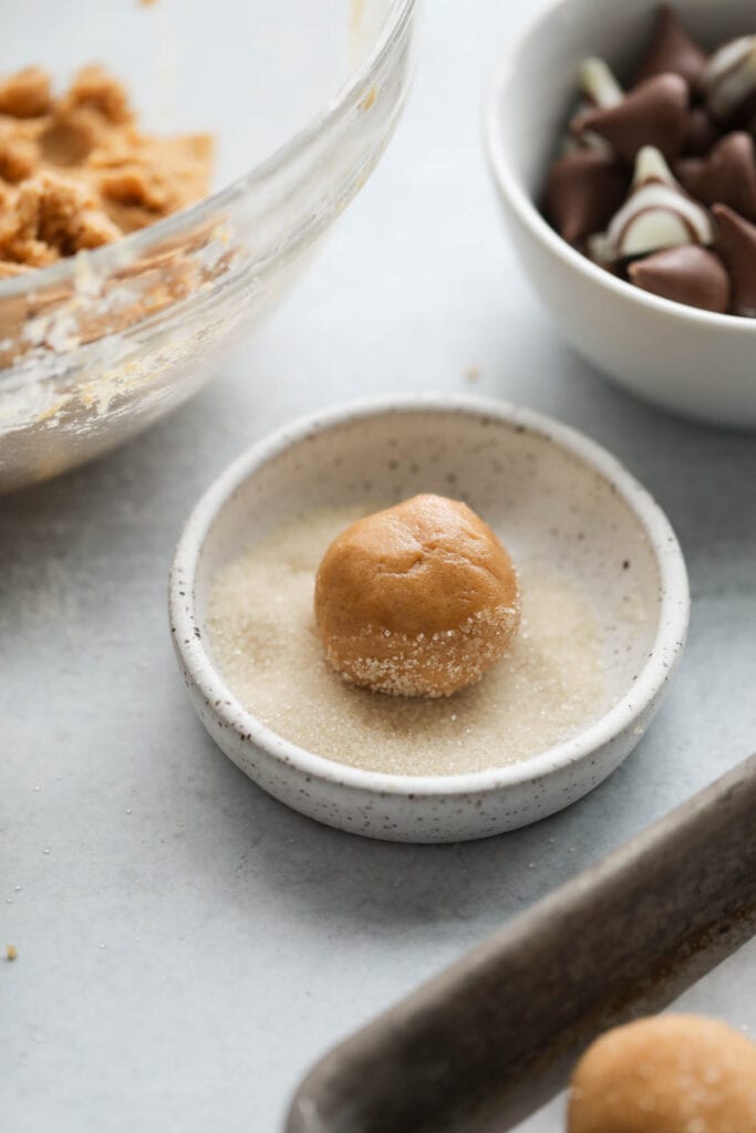 Peanut butter blossom cookie dough ball in a shallow bowl of sugar.