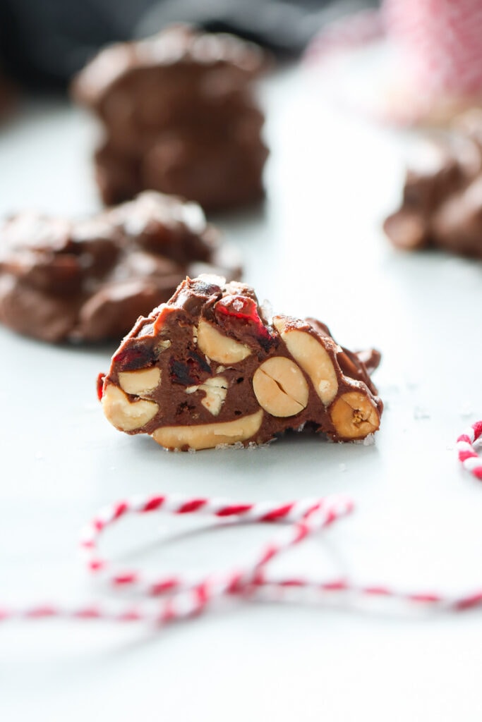 A single peanut chocolate cluster cut in half to show cocktail peanuts and dried cranberries on the inside.