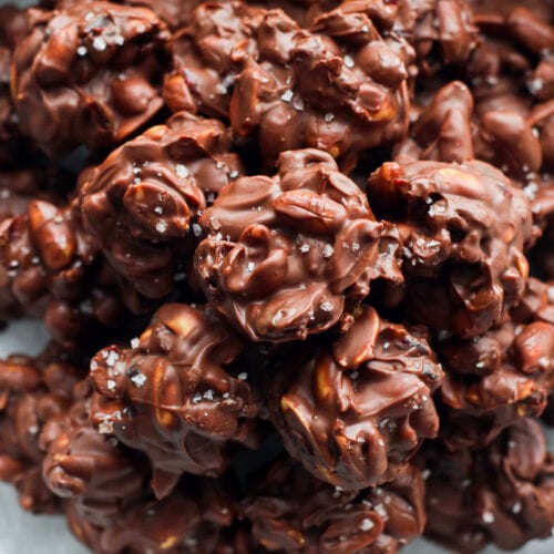 Crockpot chocolate peanut clusters piled in a parchment lined tin sprinkled with sea salt.