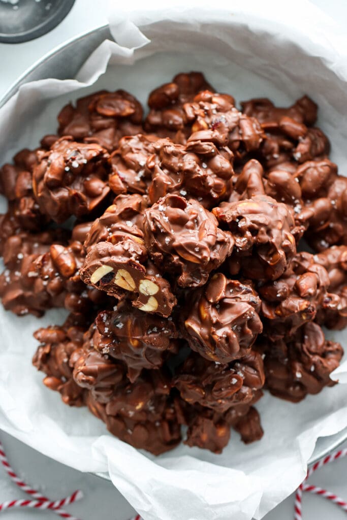 Overhead view chocolate peanut butter clusters piled up high in a tin sprinkled with sea salt.