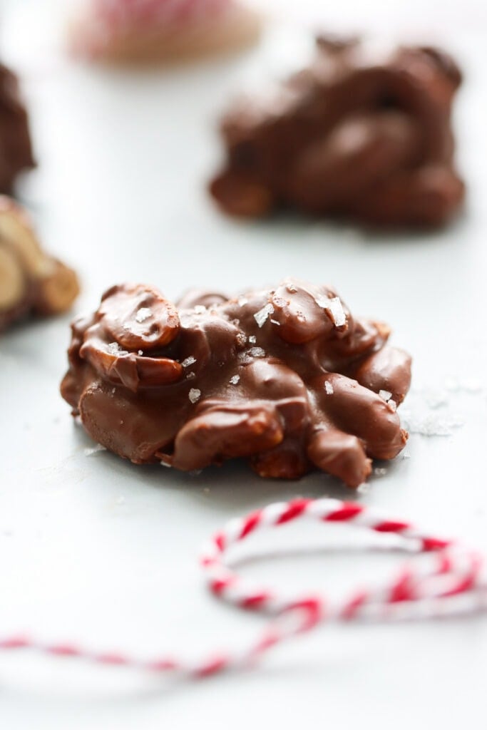 Close up view single crockpot peanut butter cluster on white counter with sea salt sprinkled over top.