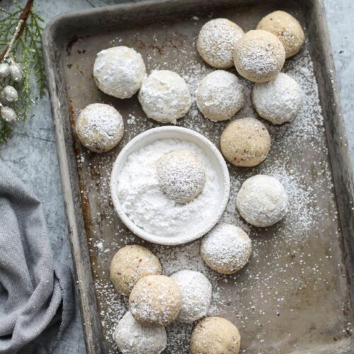 Overhead baking sheet with several pecan snowball cookies dusted in powdered sugar.